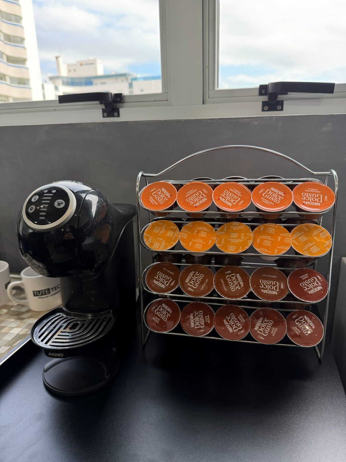 Máquina de café, caneca da Tute Tech e cápsulas no balcão da loja