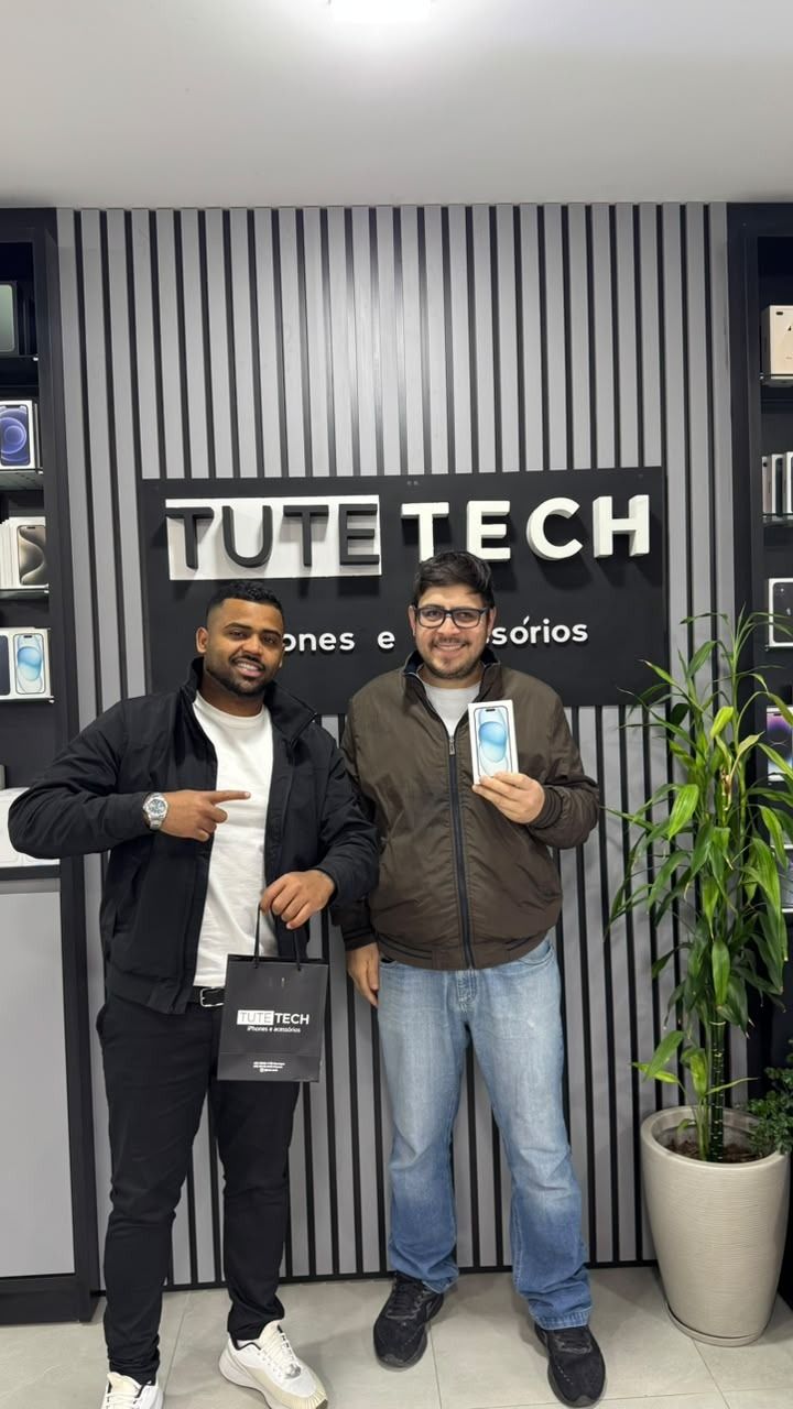 Cliente segura o iPhone novo ao lado do consultor, em frente ao painel da Tute Tech