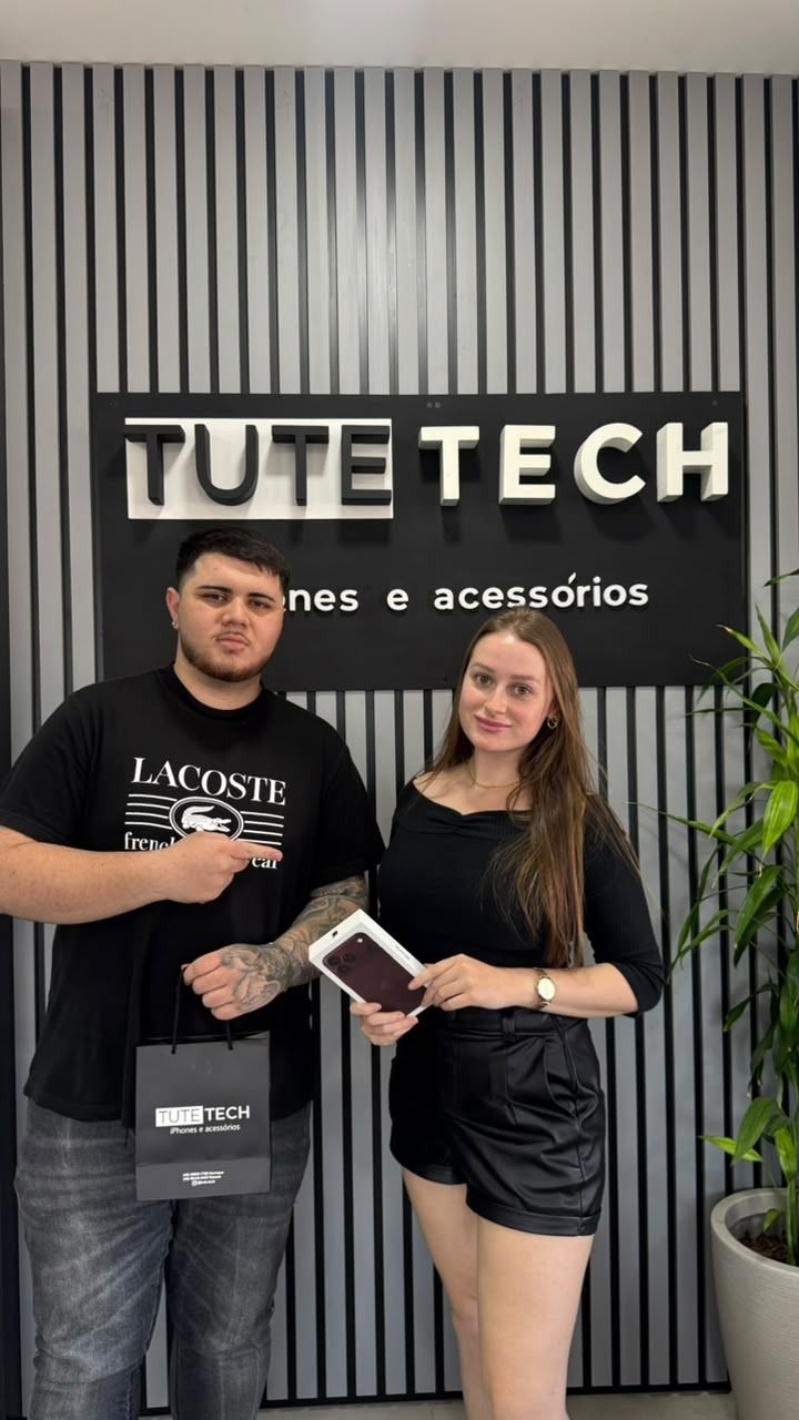 Cliente segura a caixa do iPhone novo, ao lado do consultor, com a sacola da loja