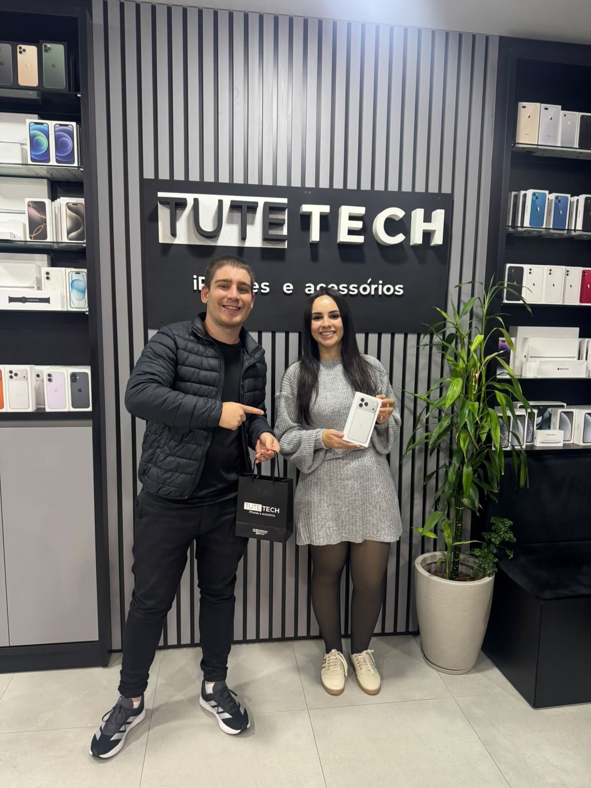 Consultor e cliente com o iPhone novo em frente ao painel com o logo da Tute Tech