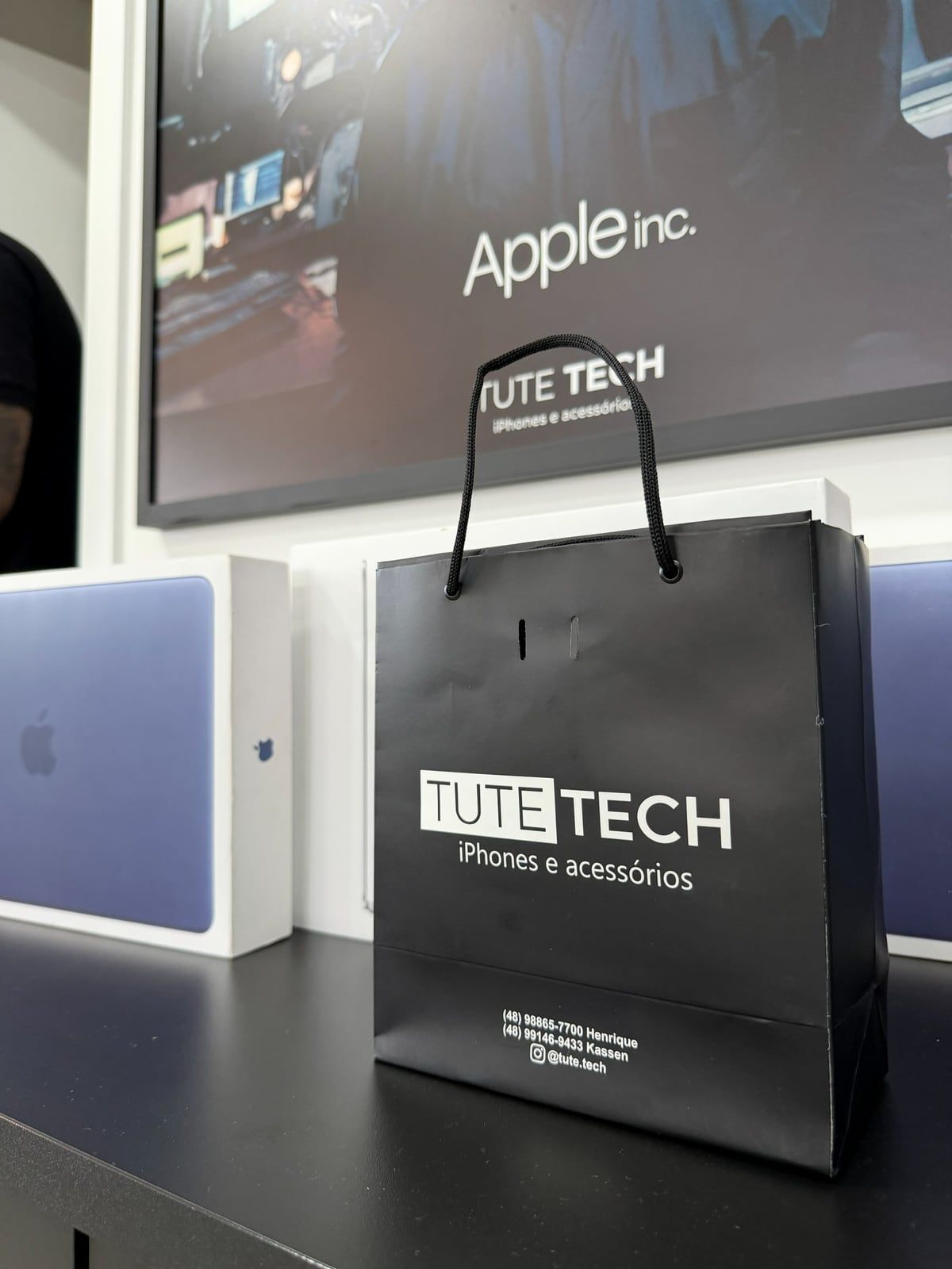 Sacola preta da Tute Tech ao lado de caixas de MacBook e iPad